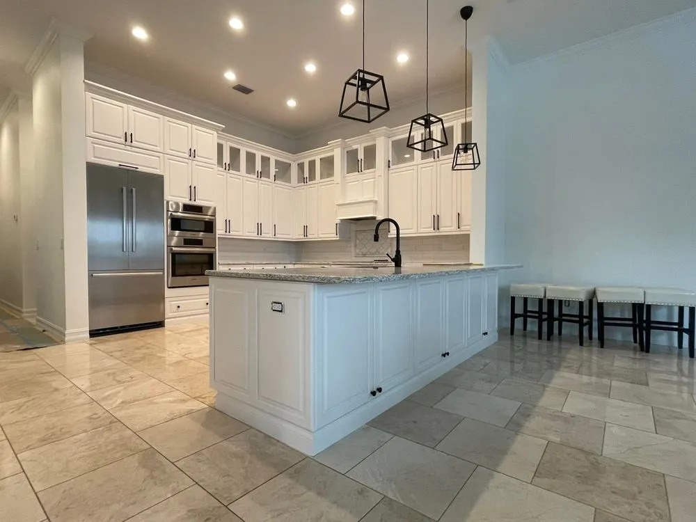 White painted kitchen cabinets and island under black pendant lights